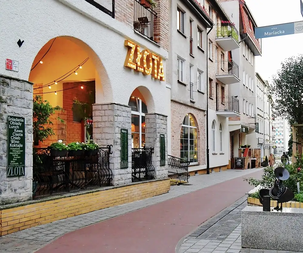 Narożna kamienica ze złotym napisem ZŁOTA nad kamienną arkadą, stoliki w ogródku na deptaku
